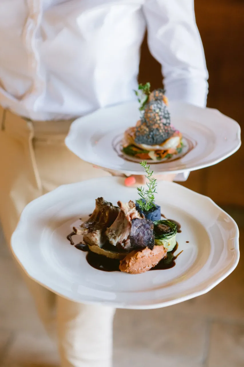Serveur portant deux assiettes gastronomiques élégantes au sein de notre Restaurant situé à Orgon